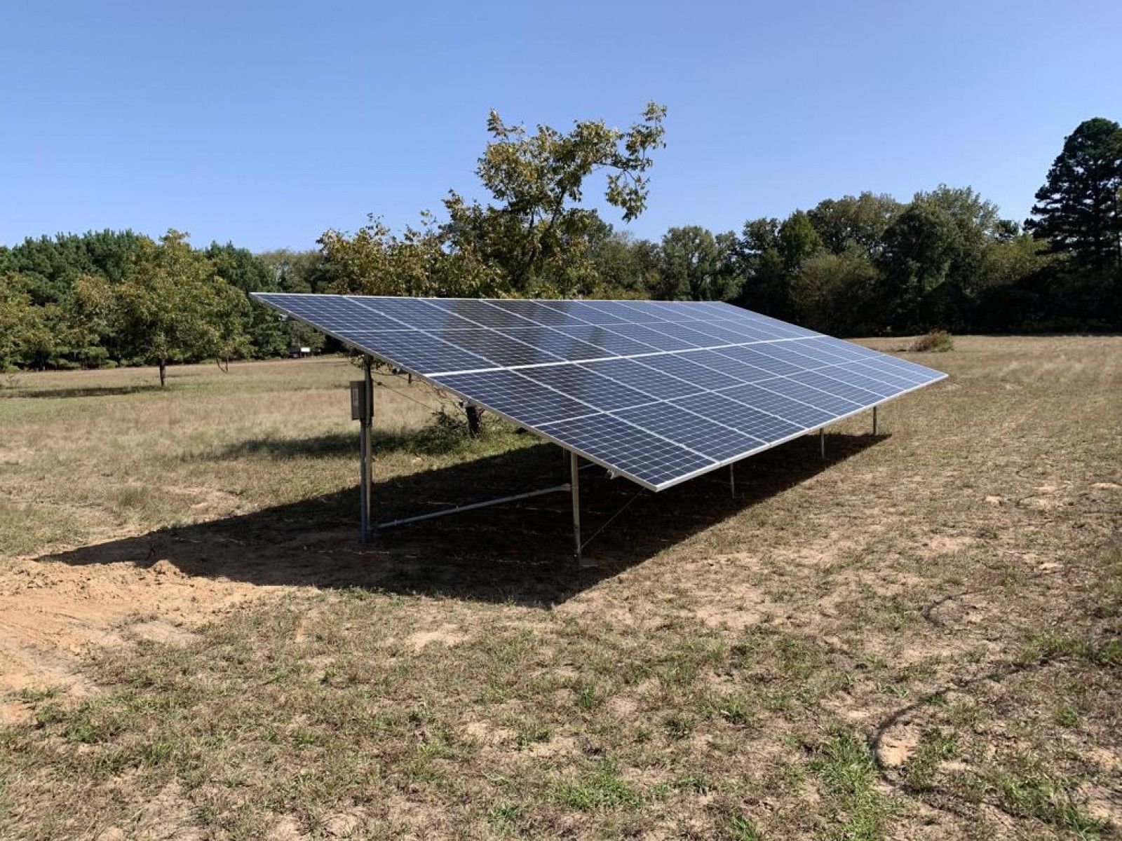 A ground-mounted solar panel array installed in a sunny, grassy field under a clear blue sky.