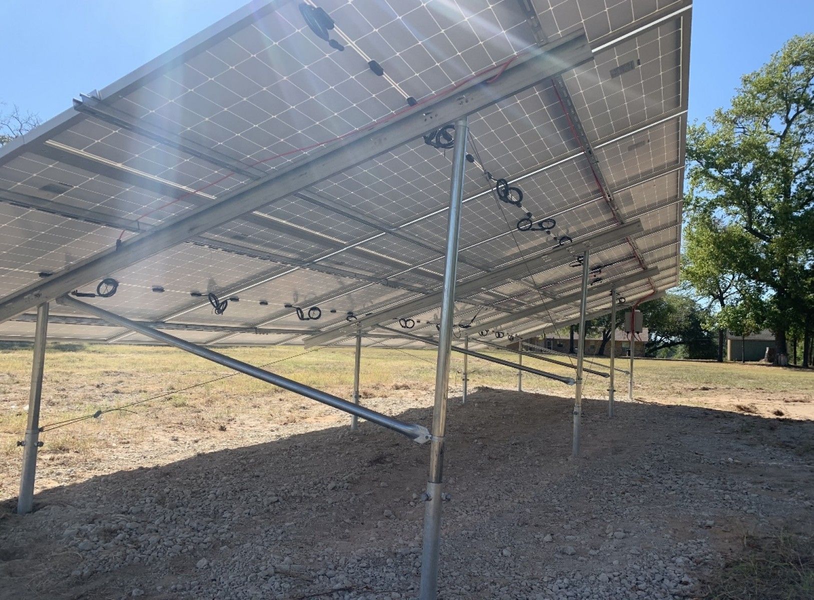 A ground-mounted solar panel array installed on a gravel field under a clear blue sky.