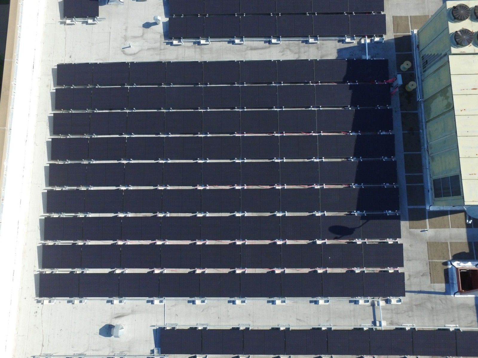 An aerial view of multiple rows of dark solar panels installed on a flat commercial rooftop.