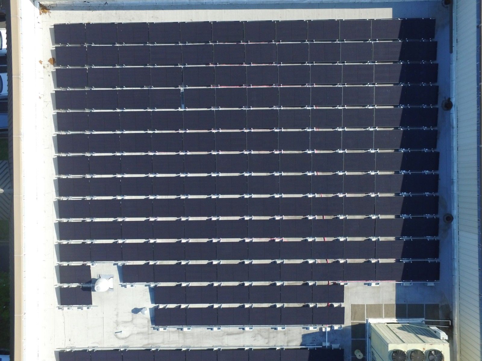A top-down aerial view of a rooftop covered with multiple rows of dark, rectangular solar panels.