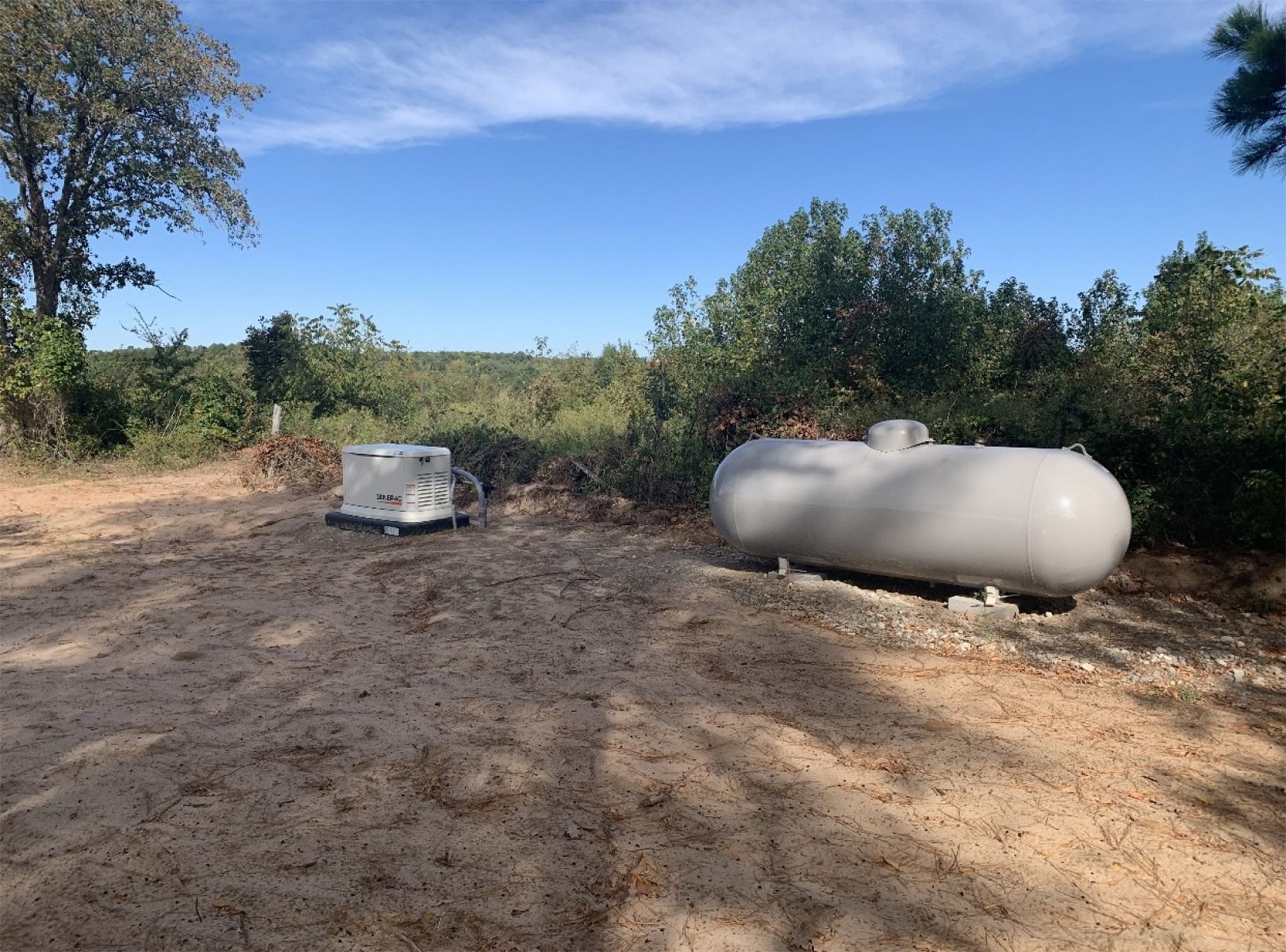 Outdoor dirt clearing with a silver propane tank and a generator under a blue sky