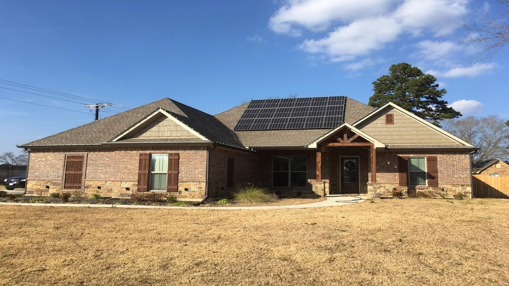 Single-story brick house with a dark roof and front porch in a dry yard under a blue sky