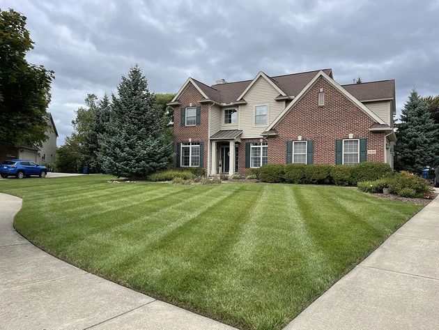 Suburban two-story brick house with a neatly striped front lawn and curved driveway under cloudy skies
