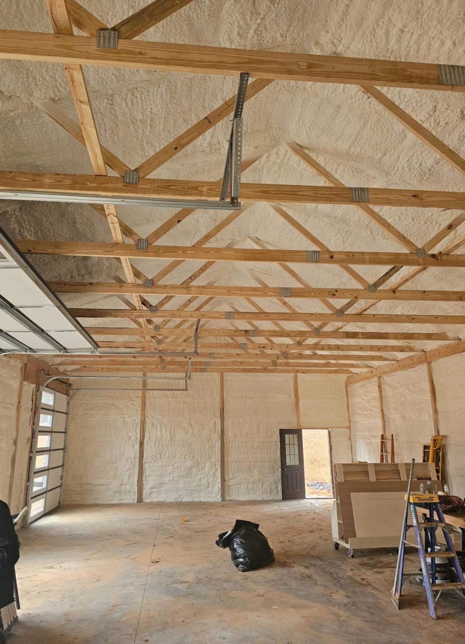 Interior of a garage insulated with spray foam; wood beams and trusses are visible.
