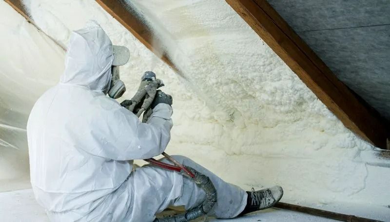 Person in protective suit spraying insulation in an attic.