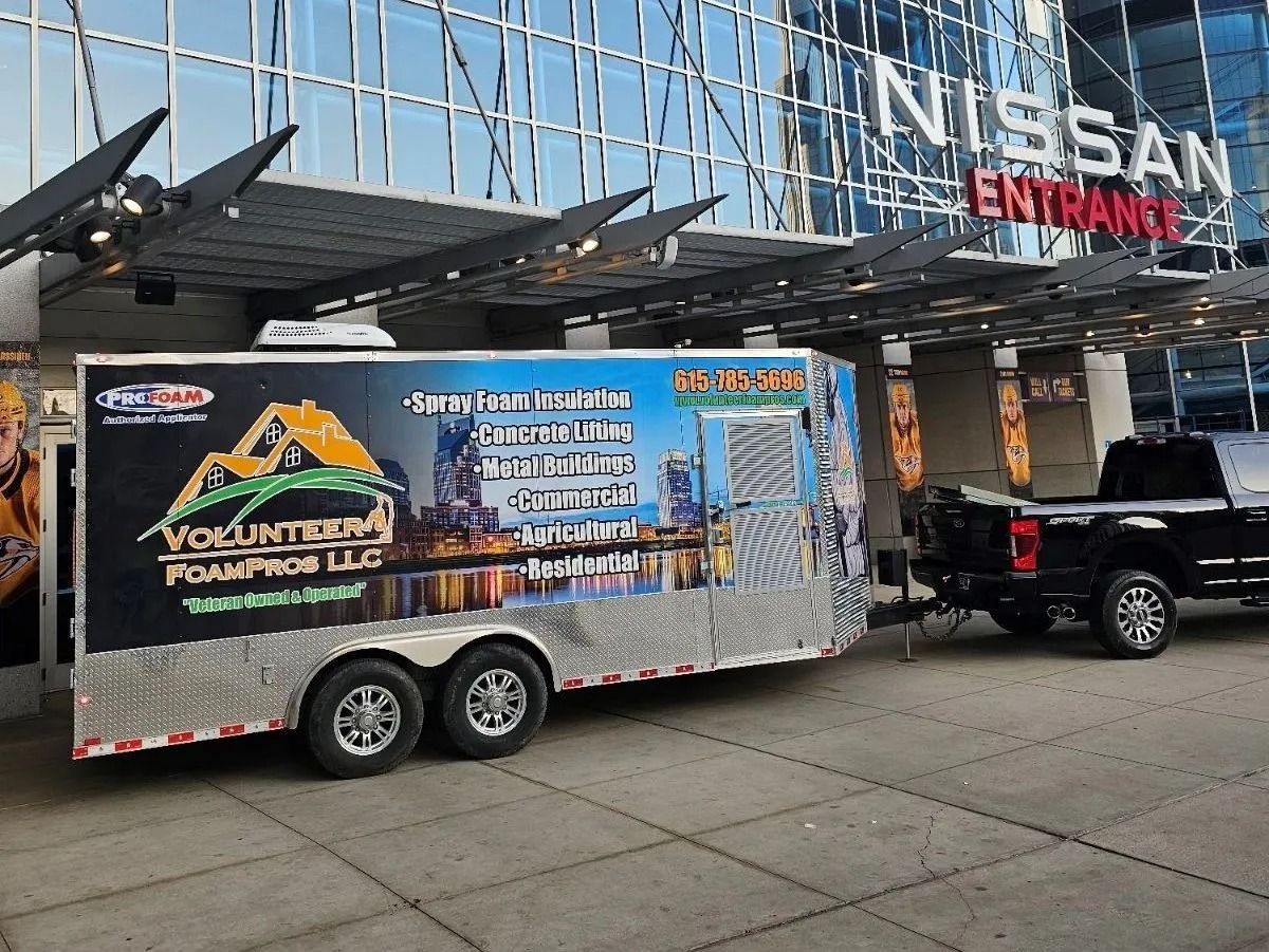 A trailer with business branding is hitched to a black pickup truck in front of the Nissan Entrance.
