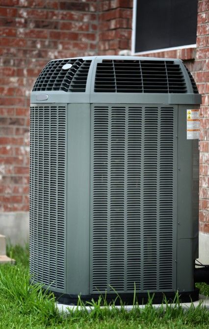 A large air conditioner is sitting in the grass in front of a brick building.