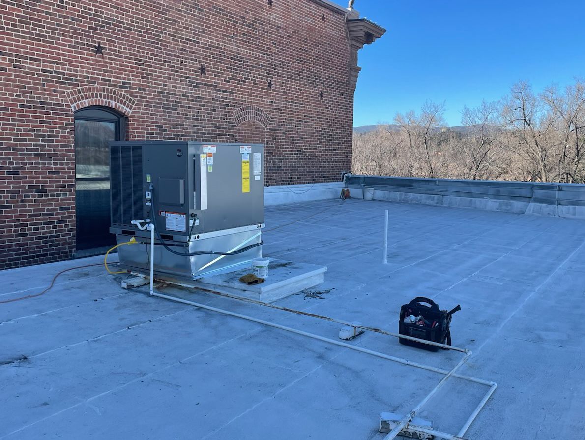 An air conditioner is sitting on top of a roof next to a brick building.