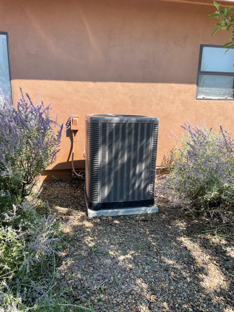 A large air conditioner is sitting in the dirt in front of a house.