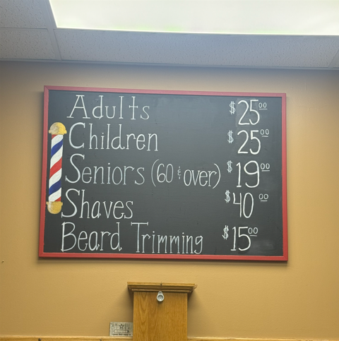 Price list on chalkboard: adult & children's haircuts $25, seniors $19, shaves $40, beard trimming $15.