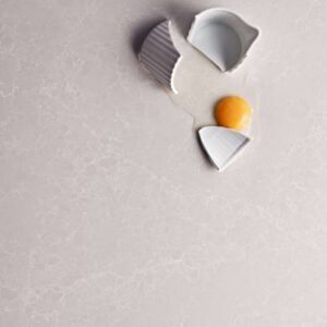 Broken eggshell with yolk on a light gray textured surface.