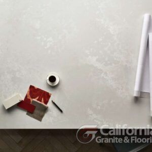 Overhead shot of a light-colored countertop with a cup of coffee, fabric swatches, and blueprints.