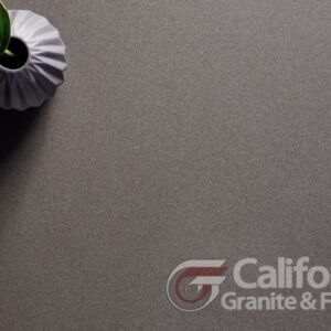 Flat lay of a dark gray granite surface with a white vase and plant in the upper left corner.