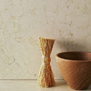 A decorative arrangement: bundled straw, wooden bowl, against a mottled beige backdrop.
