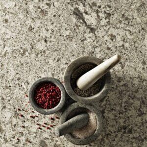 Three stone mortars with red and black peppercorns, and pestles on a speckled, stone countertop.