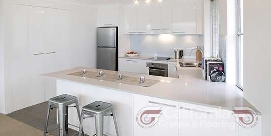 Modern white kitchen with stainless steel appliances and bar stools.