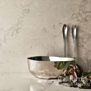 Stainless steel bowl with utensils and salad on a marble countertop.