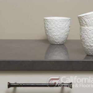 Gray countertop with white patterned cups, and dark cabinet pull.