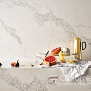 Countertop with fruit, a juicer, and a golden pitcher against a marbled white backdrop.