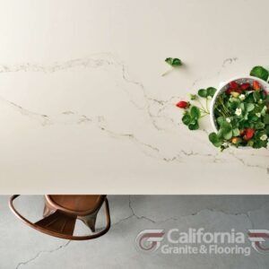 White countertop with a bowl of strawberries and a chair. California Granite & Flooring logo.