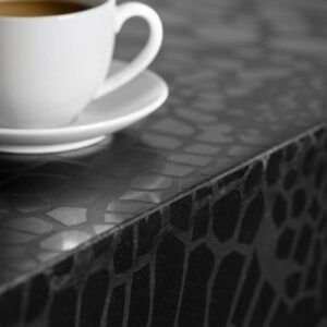 White coffee cup on a saucer, on a dark, patterned countertop.