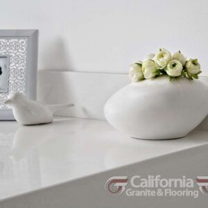 White vase with flowers, bird figurine, and picture frame on white surface.