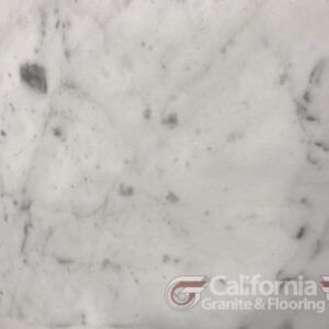 White marble slab with gray veining and dark spots.