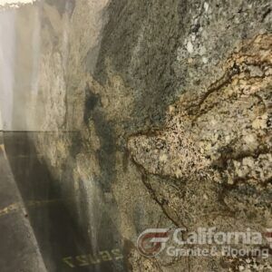 Close-up of a granite slab, showing a mix of browns, golds, and grays. The polished surface reflects light.