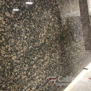 Close-up of a polished granite slab with a mottled pattern of brown, tan, and black spots, reflecting light.