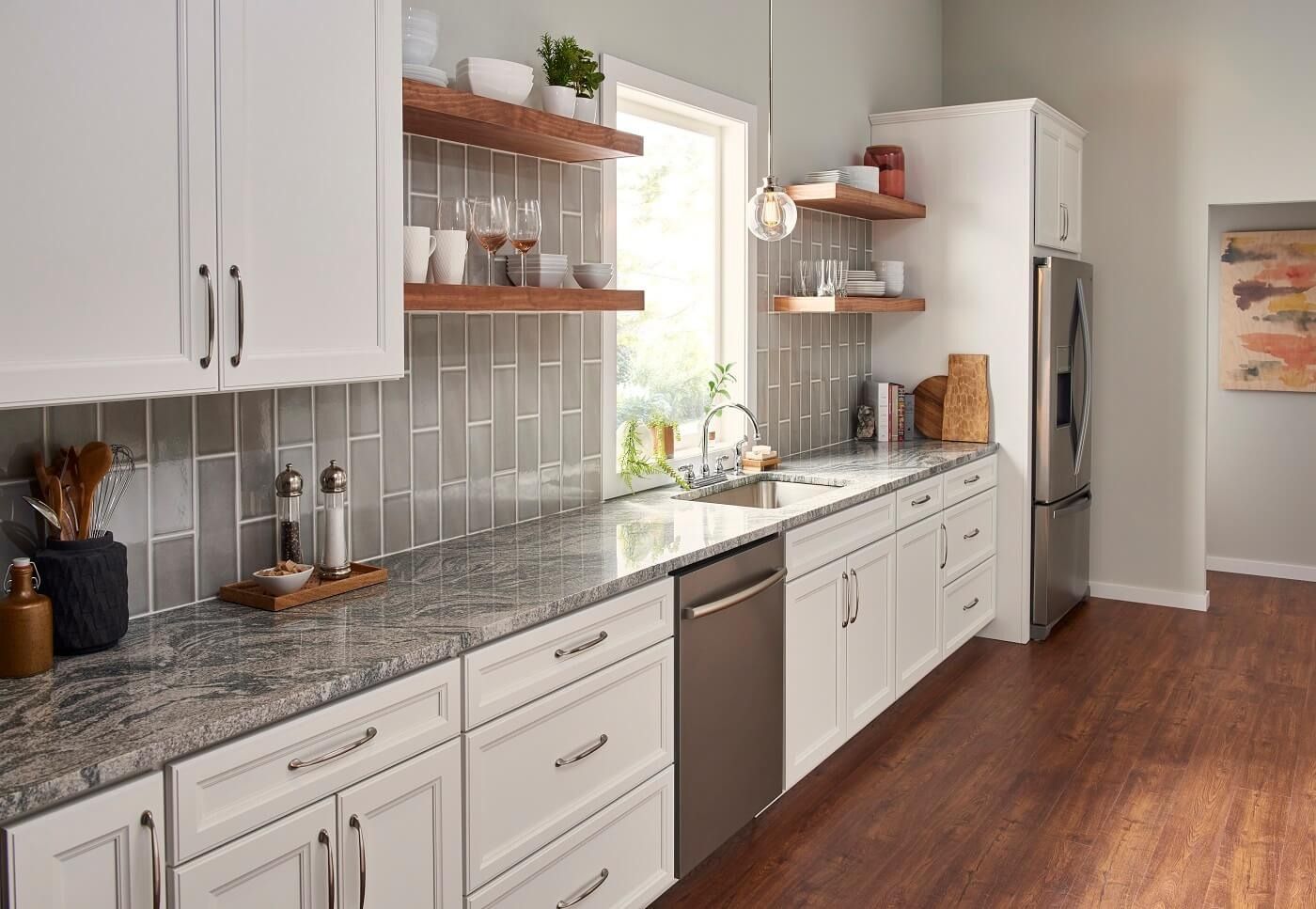 Bright kitchen with white cabinets, a stainless steel dishwasher and refrigerator, and gray granite countertops. Open wooden shelves flank a window above the sink.
