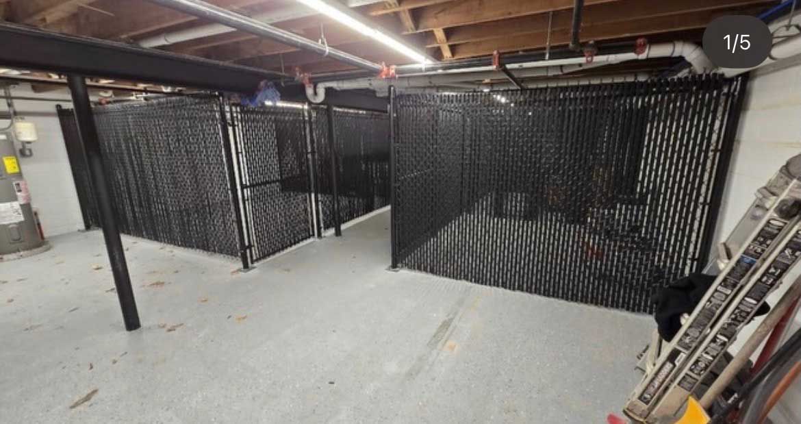 Black chain-link fence partitions an indoor space with a gray floor and exposed beams.