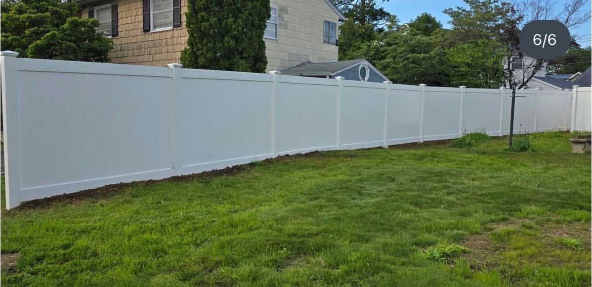 White vinyl privacy fence in a grassy yard, with a house visible in the background.