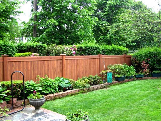 Brown fence surrounding a green lawn with flowerbeds and lush trees.