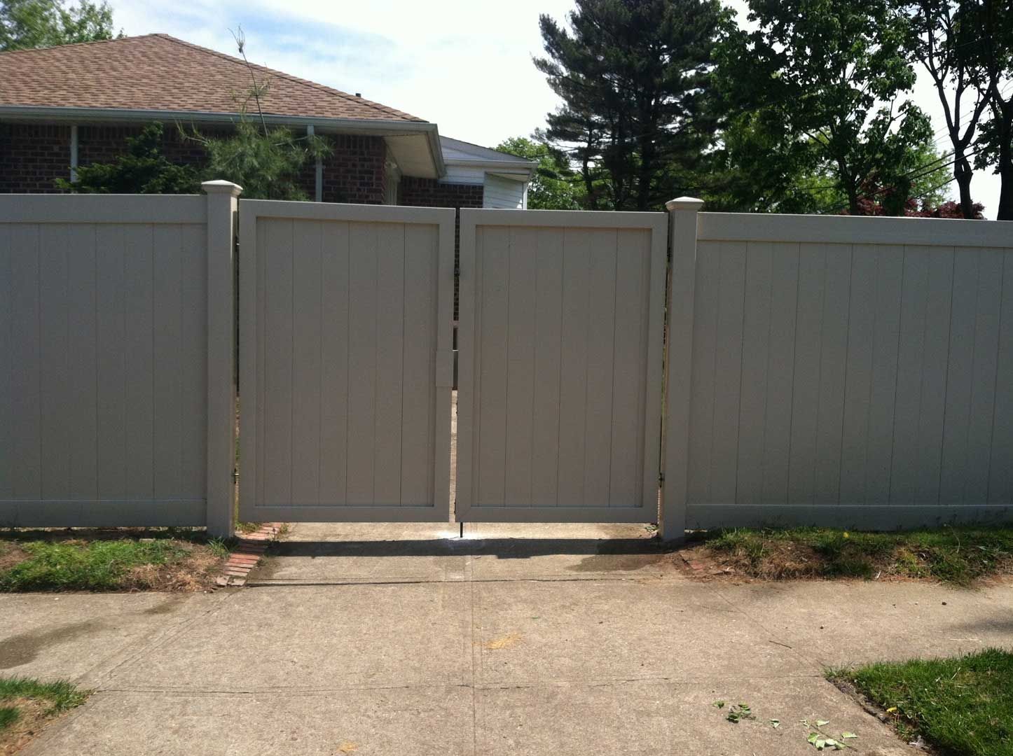 Closed beige vinyl gate in a matching fence, fronting a sidewalk and lawn.