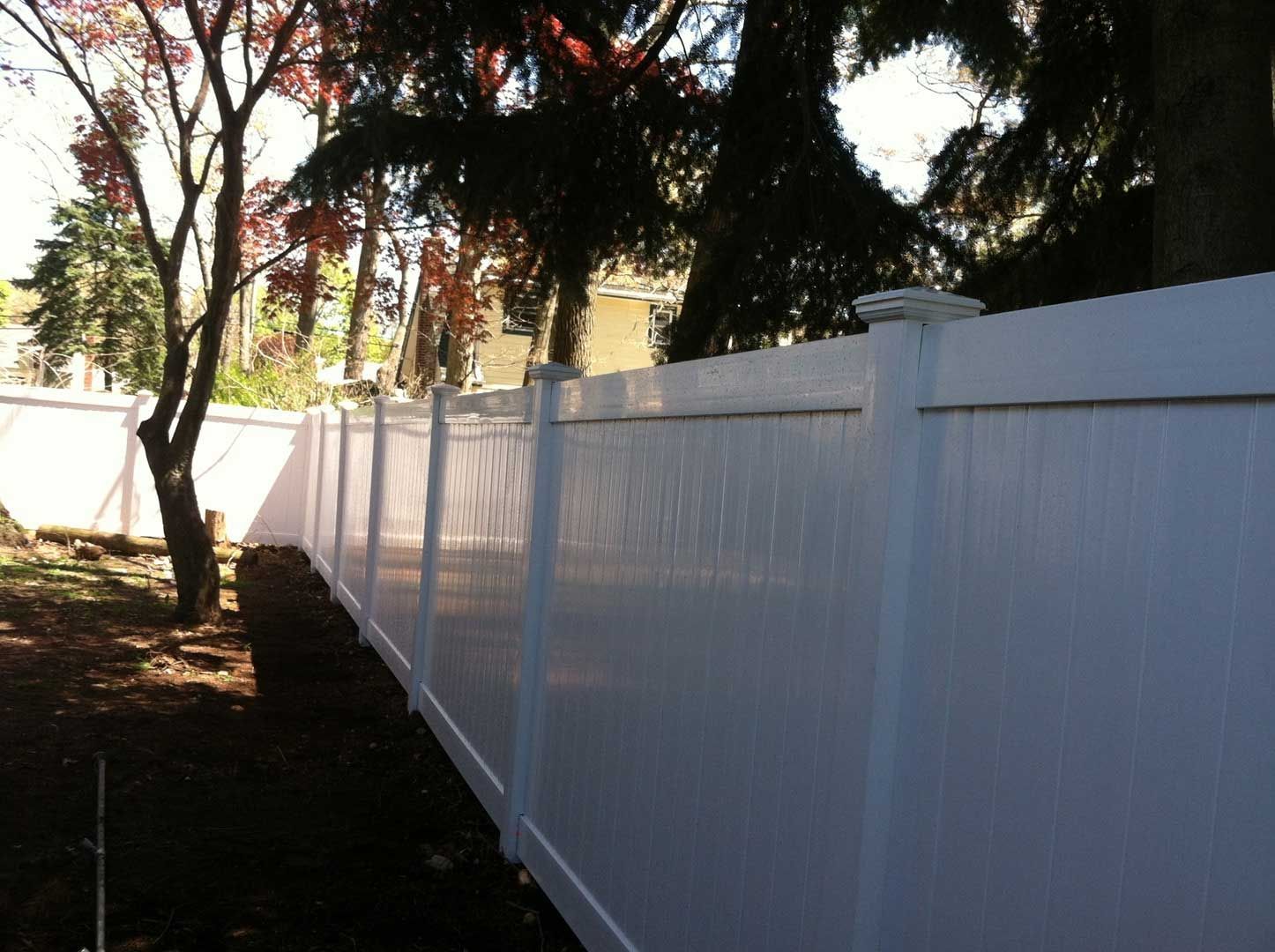 White vinyl fence in a backyard, with trees and sunlight.