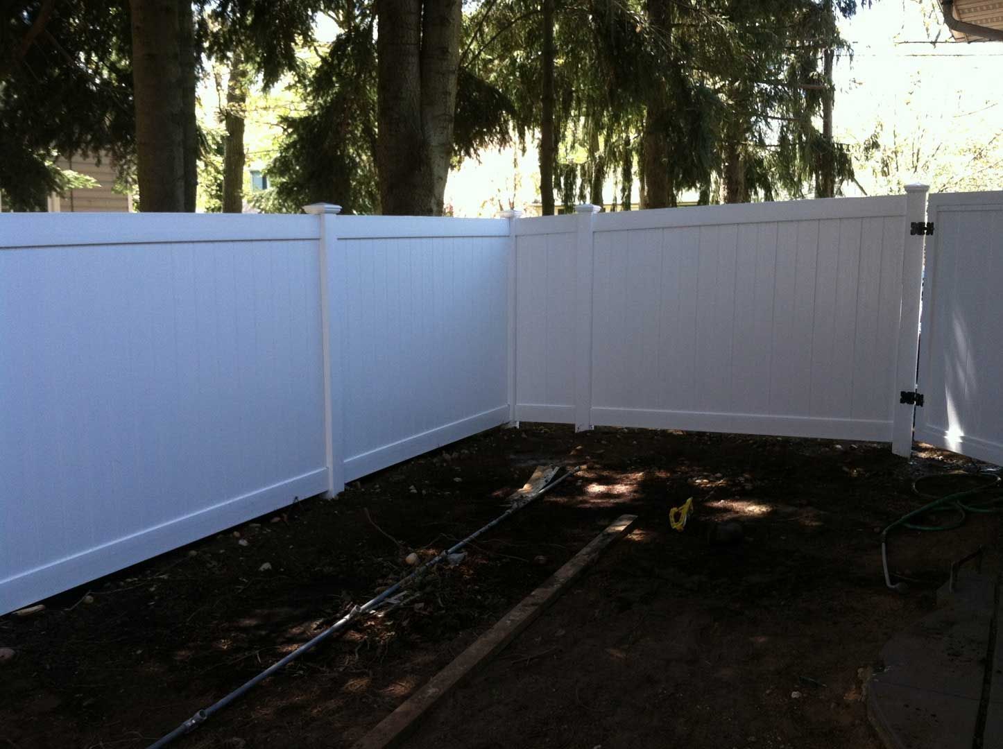 White vinyl fence encloses a small yard. Trees in the background.
