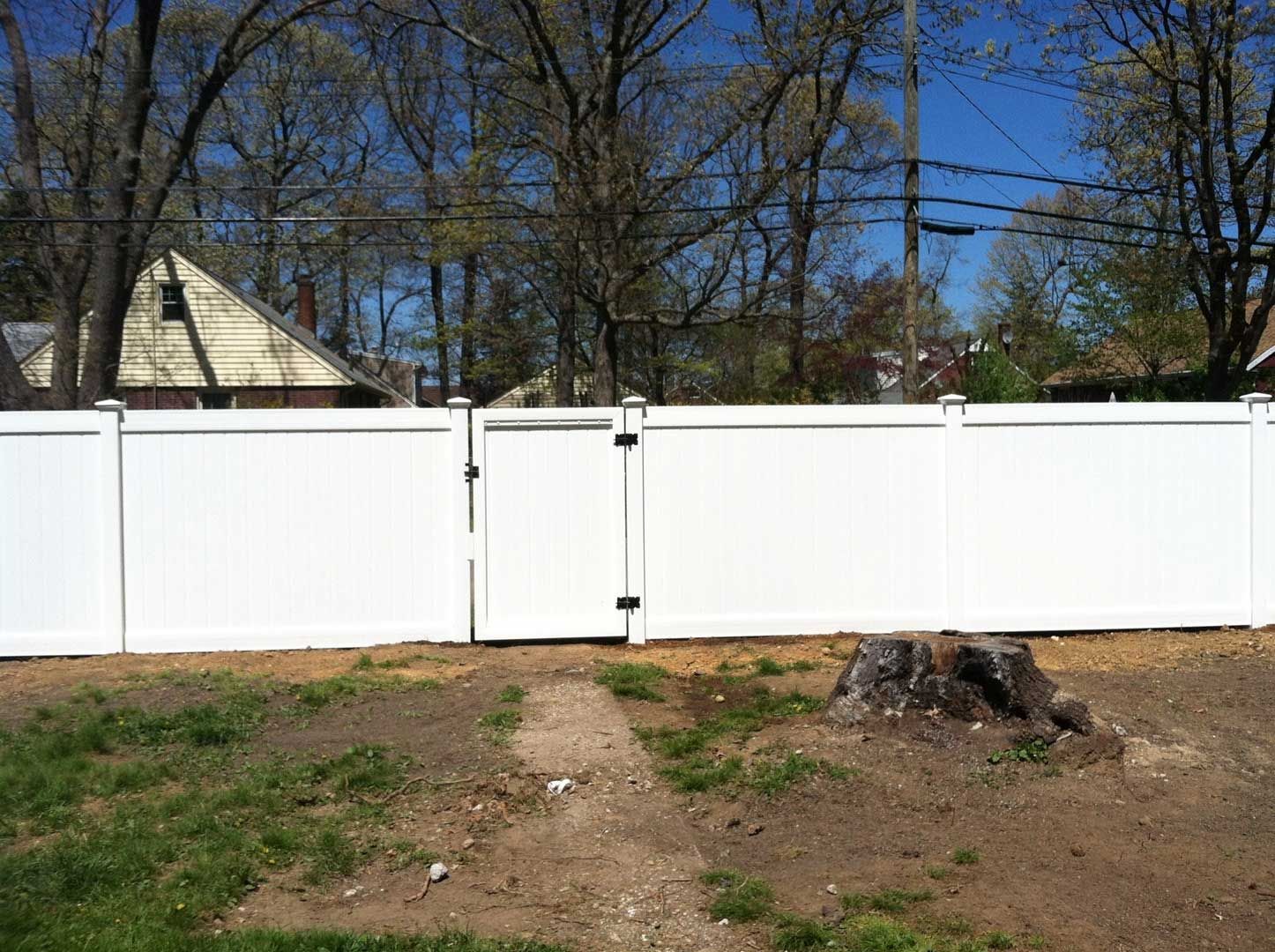 White vinyl fence with a gate in a grassy backyard.