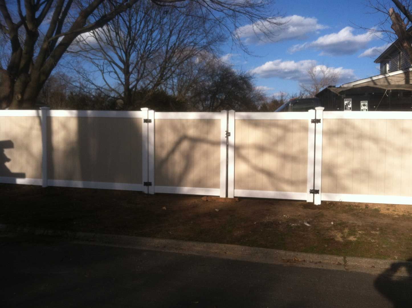 Tan and white vinyl fence with two gates, under a partly cloudy blue sky.