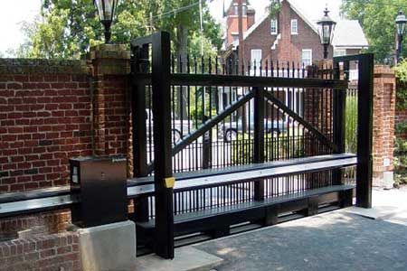 Black metal sliding gate, brick pillars, and a building in the background.