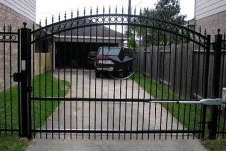 Black metal driveway gate, arched top, automated arm, leading to a garage.