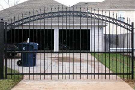 Black wrought iron driveway gate arched over a concrete driveway, leading to a garage.