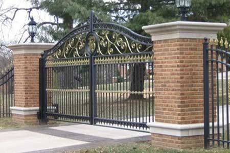 Ornate black metal gate with gold detailing, between brick pillars with lights.