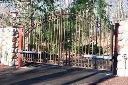 Iron driveway gate with ornate design between stone pillars.