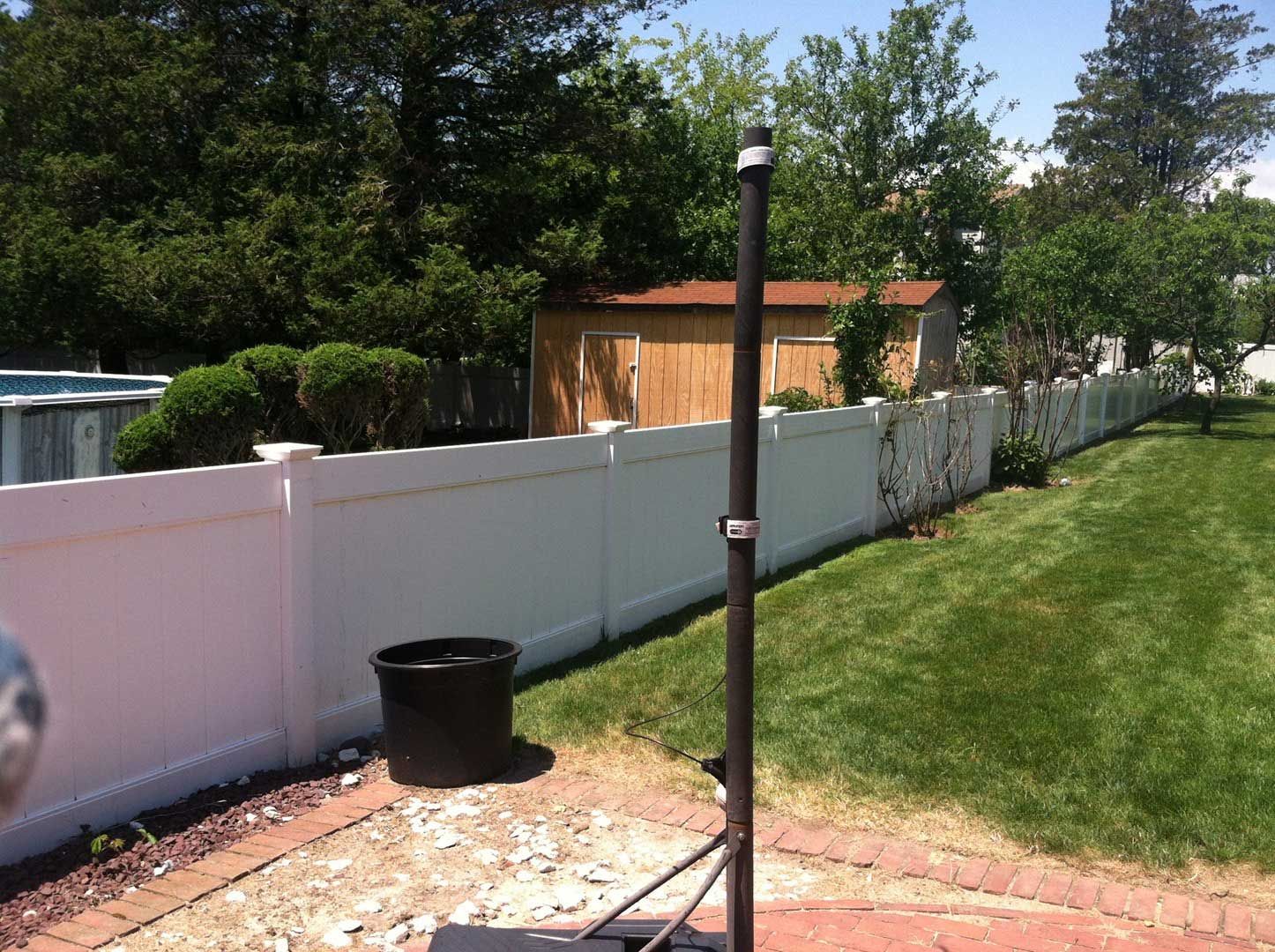 White fence in a backyard with a shed and trees in the background under a blue sky.