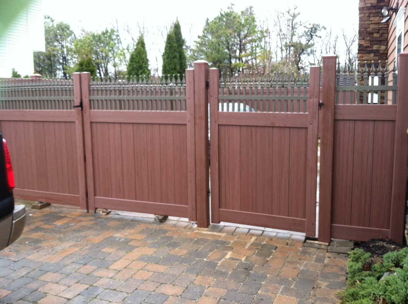 Brown wooden gates in a brick driveway, leading to a fenced backyard.