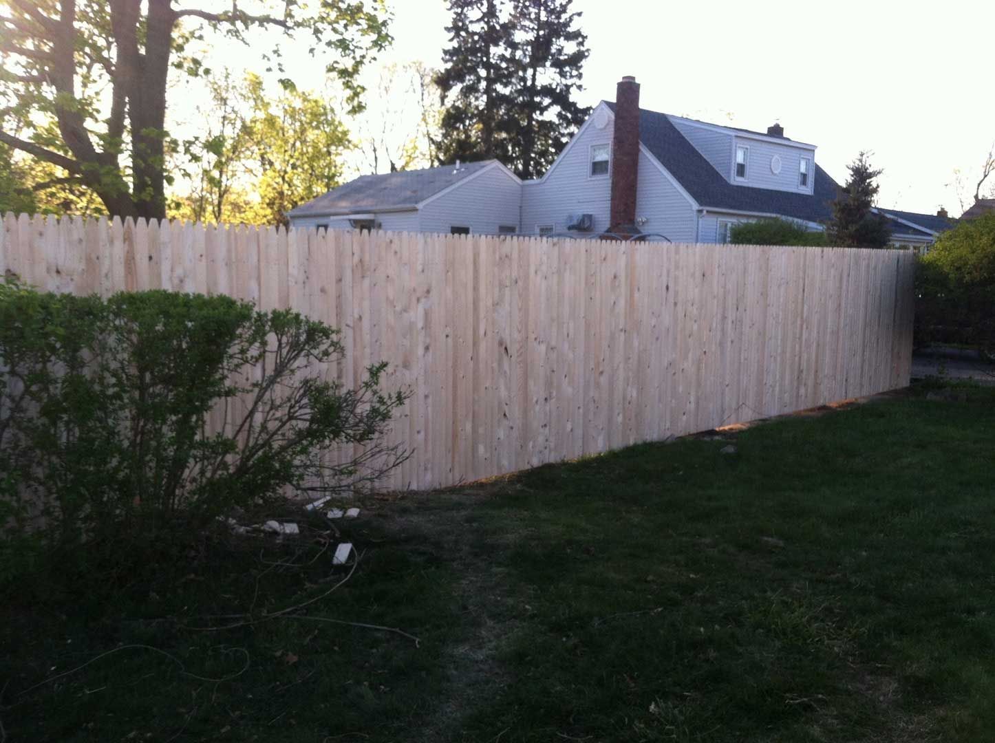 Wooden privacy fence in a backyard, with a house in the background and a green lawn in the foreground.