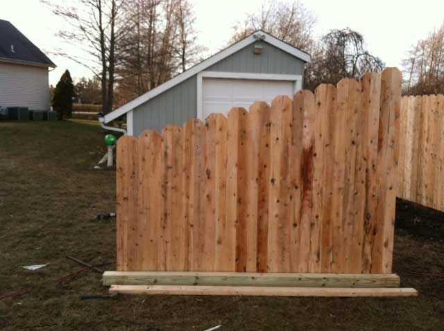 Wooden fence with scalloped top in backyard, near a garage and house.
