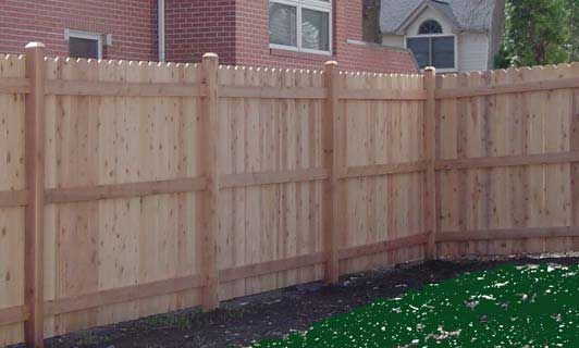 Wooden fence surrounding a yard, brick building in the background.