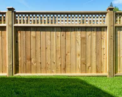 Wooden fence with lattice top, set in green grass, under blue sky.