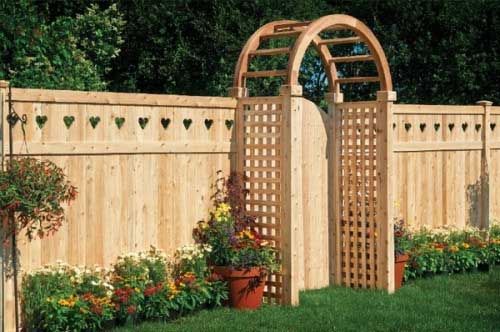 Wooden fence with heart cutouts, arched gate, and flowerbeds.
